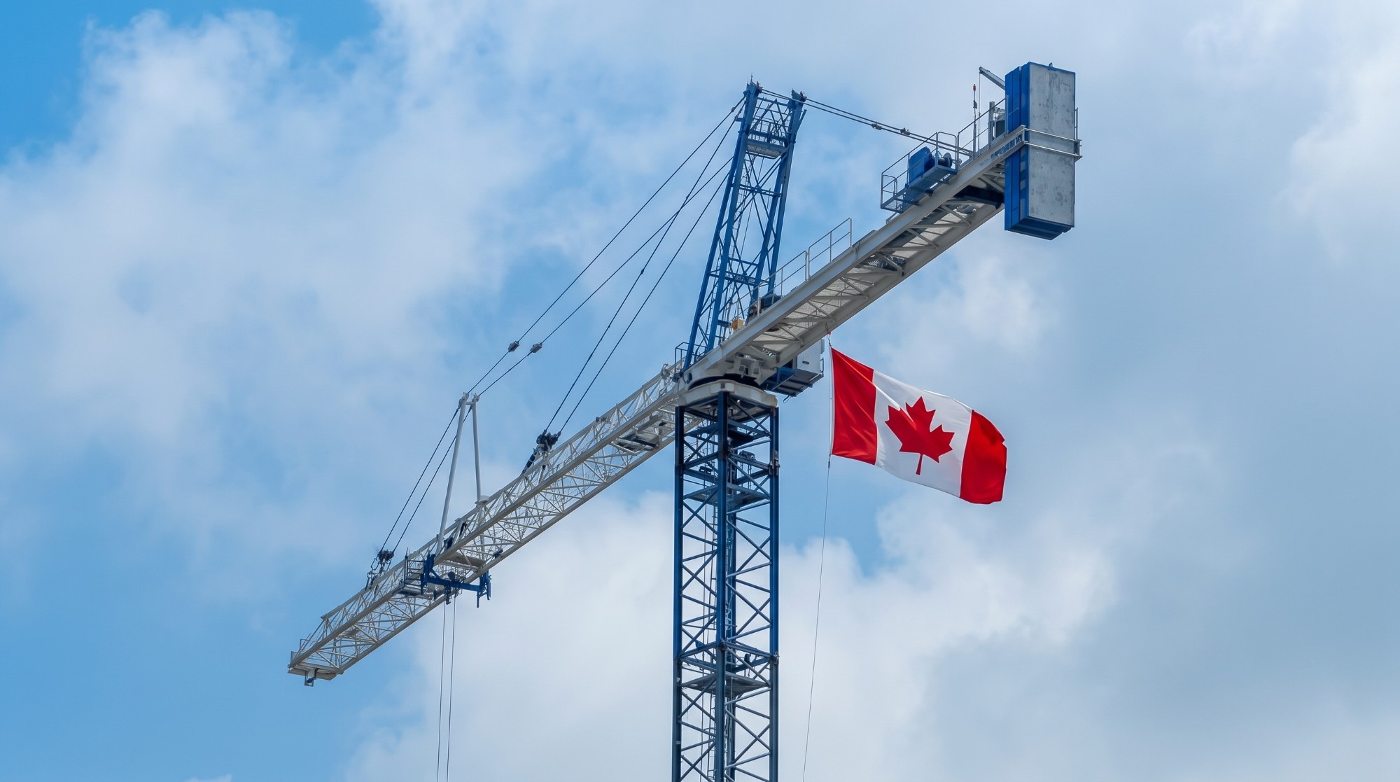 A tower crane against a blue sky, with the Canadian flag flying from its mast
