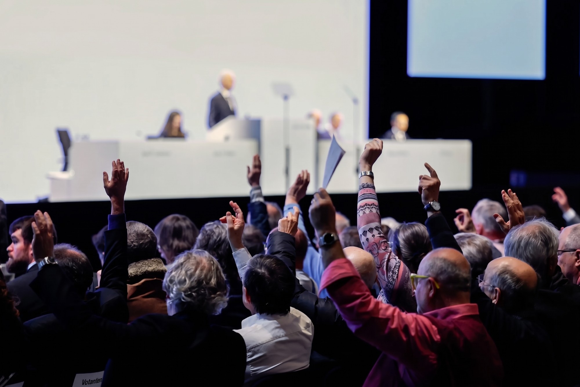 Shareholders raising their hands to vote at a general meeting